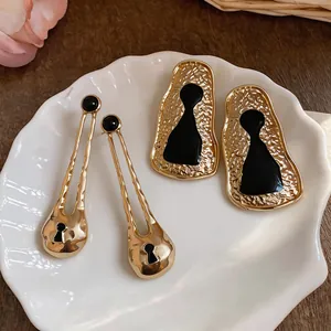Close-up of gold-colored geometric earrings with unique black resin keyhole designs.