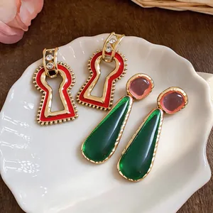 Vintage green resin waterdrop and red keyhole drop earrings on a white shell plate.