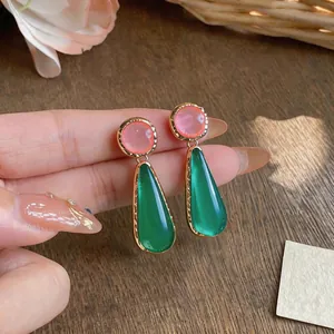 Macro detail of resin teardrop earrings with pink and green contrast in gold plating.