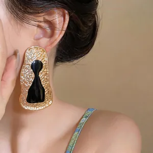 Exaggerated golden geometric keyhole earrings with black resin detail on model's ear