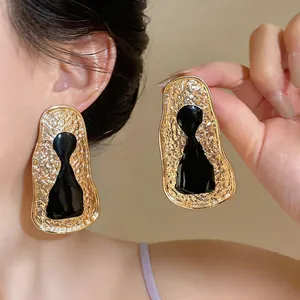 Detailed view of oversized golden geometric earrings with black keyhole resin inlay