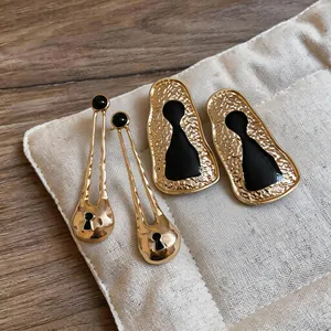 Detailed view of gold earrings with black resin keyhole design on beige pad