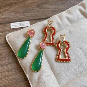 Detailed view of vintage-style resin teardrop and red keyhole-shaped earrings on a fabric pouch.