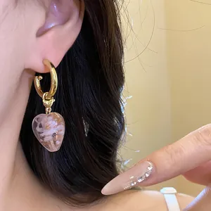 Nahaufnahme eines goldenen Kreolen-Ohrrings im Vintage-Stil mit Herzanhänger aus Glas.