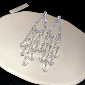 Detalle de pendientes largos de plata con circonitas brillantes y perlas elegantes
