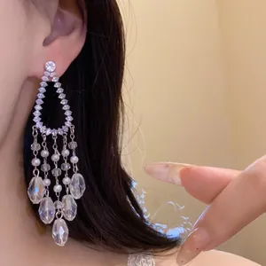 Primer plano de elegantes pendientes largos de aguja de plata con circonitas y perlas.