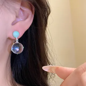 Close-up detail of mint green stud earrings with a clear glass ball drop on ear
