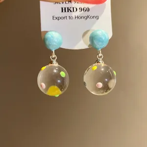 Macro detail of clear glass ball pendant earrings with colorful dots and blue studs