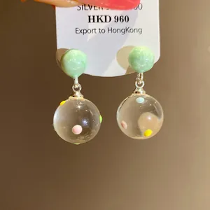 Detail of ice transparent glass sphere earrings with colorful polka dots and silver needle