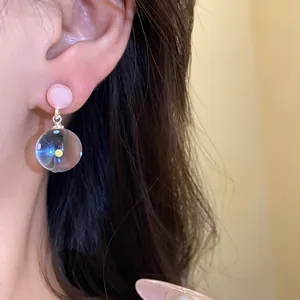 Close-up detail of a transparent dot ball pendant earring worn on a person's ear.
