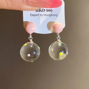 Detail shot of clear spherical drop earrings with colorful polka dots and pink studs.