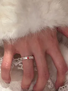 Primo piano di un delicato anello in pizzo argentato con ciondolo a fragola su un dito.