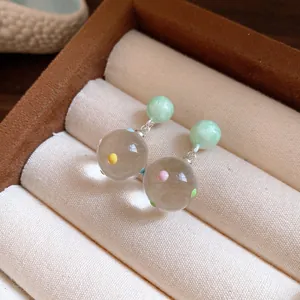 Close-up of elegant clear glass sphere earrings with colorful polka dots and green studs