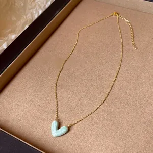 Detailansicht eines marmorierten hellblauen Herzanhängers an einer feinen Goldkette