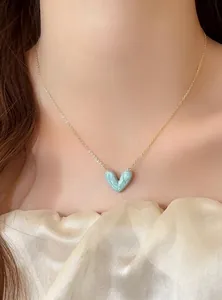 Nahaufnahme eines marmorierten hellblauen Herzanhängers an einer feinen Goldkette