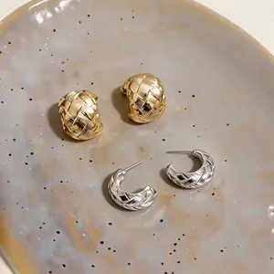 Detailed macro view of woven gold and silver C-shaped hoop earrings on a ceramic plate