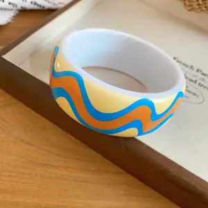 Detailed close-up of a stylish resin bangle with a vibrant blue and orange wave print.