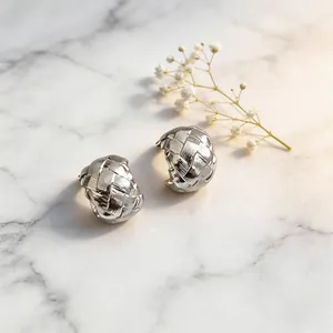 Close-up of silver metallic woven C-shaped clip-on earrings placed on marble with flowers.