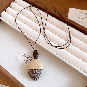 Dettaglio di un pendente a forma di ghianda su una lunga collana a cordoncino marrone