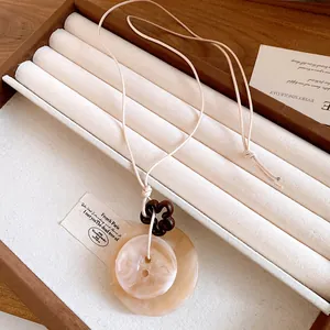 Dettaglio di ciondolo irregolare in resina con fiore in legno su collana in stile neo-cinese