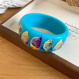 Detail shot of a vibrant blue resin bangle featuring colorful tropical fish prints
