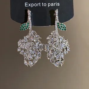 Detailed close-up of leaf-shaped silver needle earrings with green and clear zirconia.