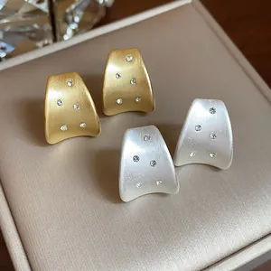 Close-up detail of elegant gold and silver brushed metal stud earrings with small zirconia stones