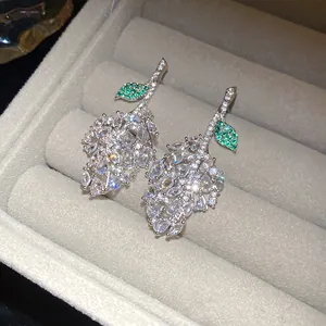 Close-up of leaf-shaped earrings featuring sparkling white and green zircons in a box