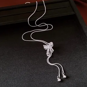 Close-up view of a silver hollow-out bow necklace with adjustable snake chain details.