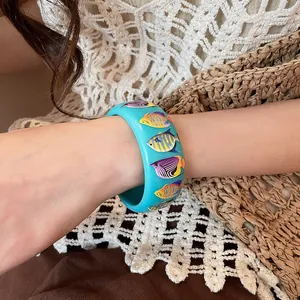 Close-up of turquoise resin bangle with colorful fish prints for seaside vacation style.
