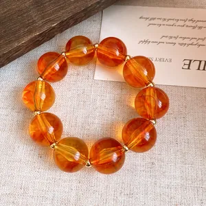 Nahaufnahme eines bernsteinfarbenen Acryl-Armbands mit goldenen Zwischenstücken.