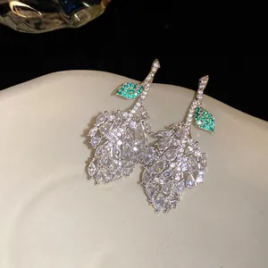 Close-up of sparkling leaf-shaped stud earrings with emerald green and clear stones