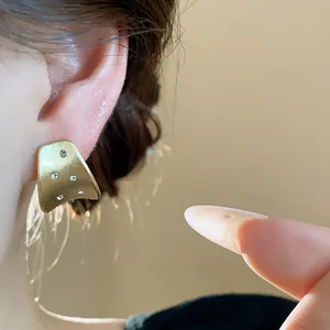 Close-up of elegant brushed gold stud earrings with sparkling zircon accents on ear.