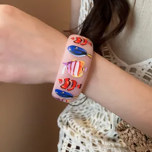 Detailed view of a pink resin bangle featuring vibrant tropical fish prints on arm