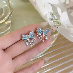 Dainty light blue zircon bow-knot stud earrings with pearl drops shown on model hand