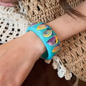 Detail shot of wide blue resin bangle featuring vibrant colorful tropical fish patterns.