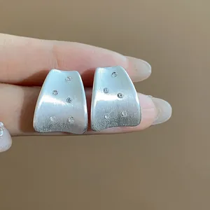 Detailed macro view of minimalist brushed silver stud earrings featuring zircon inlays