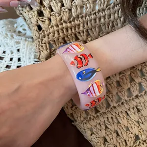 Detailed view of a pink resin bangle with colorful tropical fish prints worn on a wrist