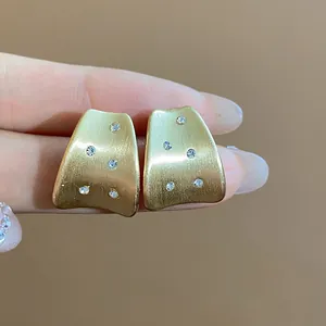 Close-up of 18k gold-plated brushed metal stud earrings with sparkling zircon accents.