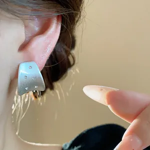Detailed view of minimalist brushed silver stud earrings with zircon stones on model