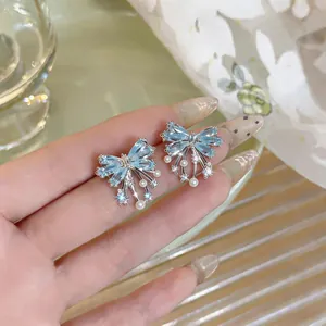 Elegant silver needle bow earrings with light blue zirconia and white pearls detail shot