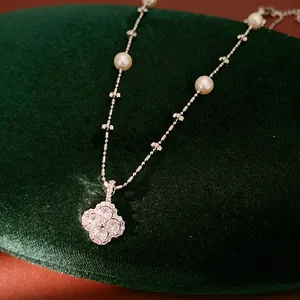 Detailed macro view of a zircon-encrusted clover pendant on a pearl beaded necklace chain
