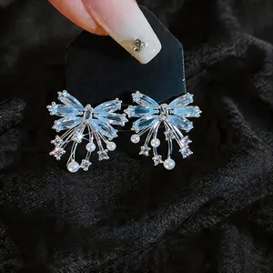 Macro view of blue butterfly zircon stud earrings with small pearls on black card.