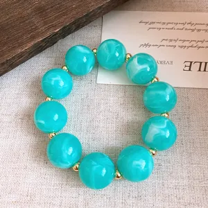 Nahaufnahme eines türkis marmorierten Acrylperlenarmband mit Goldakzenten auf Stoff