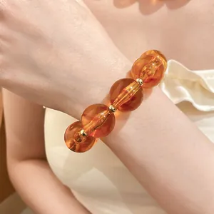 Detaillierte Nahaufnahme eines eleganten bernsteinfarbenen Acryl-Perlenarmbands am Handgelenk.