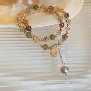 Nahaufnahme eines zweilagigen Perlenarmbands mit Goldmünze und rosa Perlenanhängern