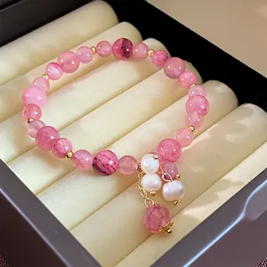 Nahaufnahme eines rosa Glasperlenarmbands mit eleganten weißen Perlenanhängern in einer Schmuckschatulle