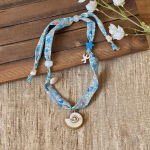 Detailed close-up of a blue fabric ribbon necklace featuring sea shell and starfish pendants.