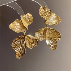 Close-up of elegant golden leaf-textured drop earrings featuring intricate ribbed patterns.