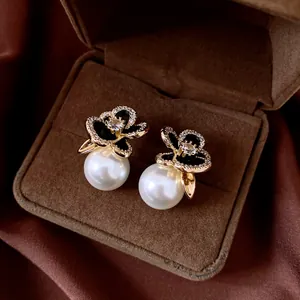 Close-up of elegant gold flower earrings with black petals and large white pearls